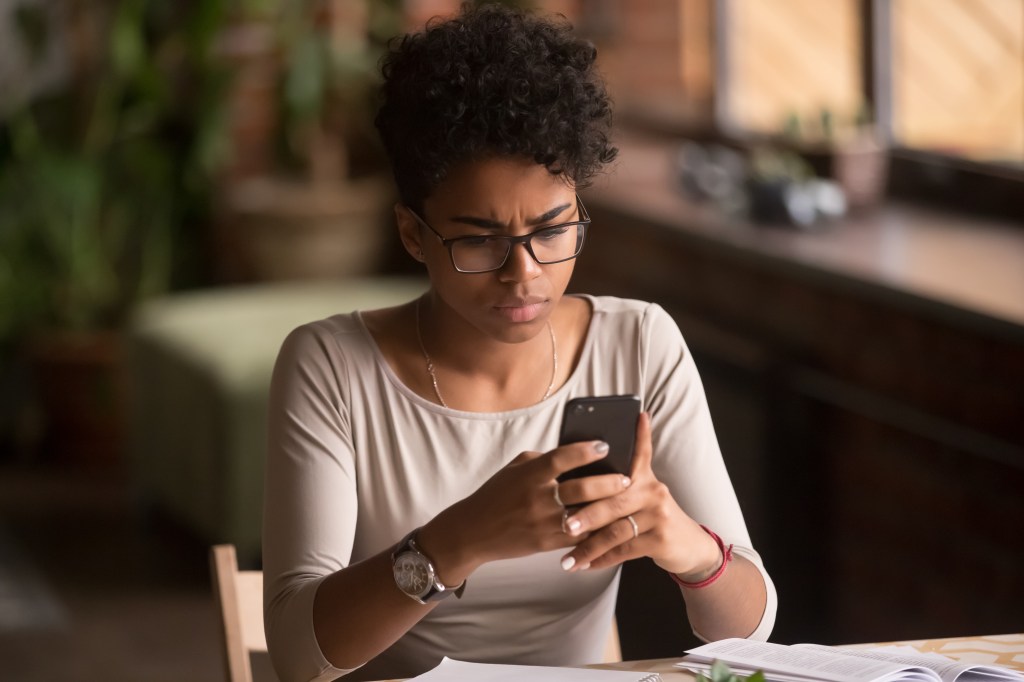 Stressed looking woman holding a cell phone while sitting at a desk