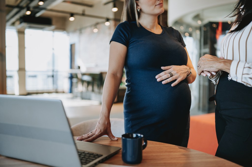 Pregnant businesswoman discussing work with colleague near a laptop