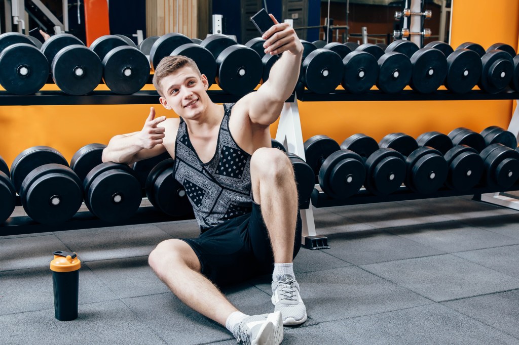 A man takes a selfie in front of a weight rack at the gym.