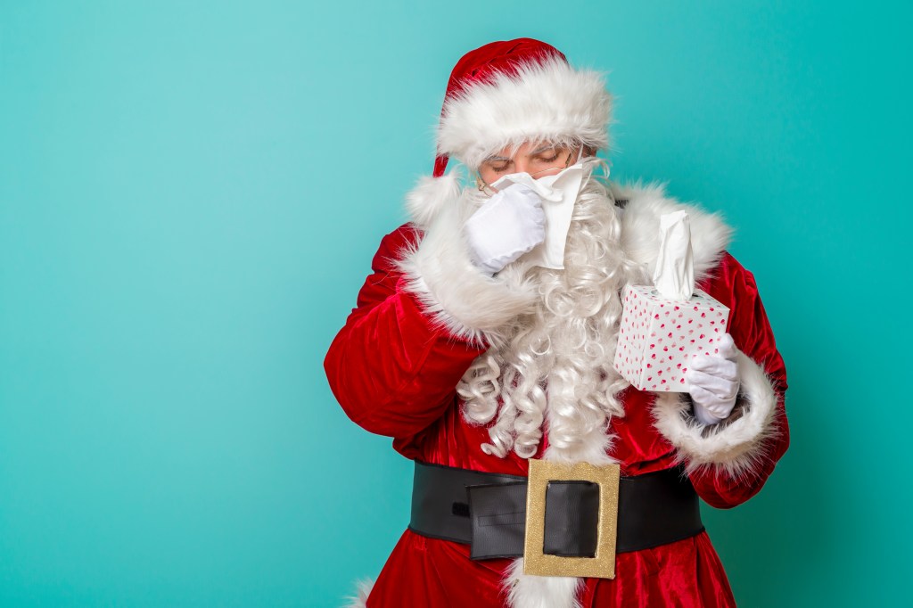 A sick Santa Claus blowing his nose and holding a box of tissues