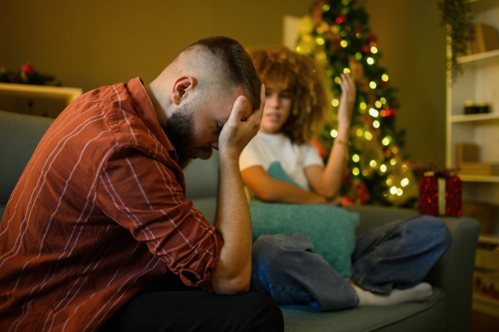 Many Americans say they are more stressed this holiday season than last year. Here, a stressed guy puts his hand on his forehead while his female partner looks on. A lit Christmas tree is in the background.