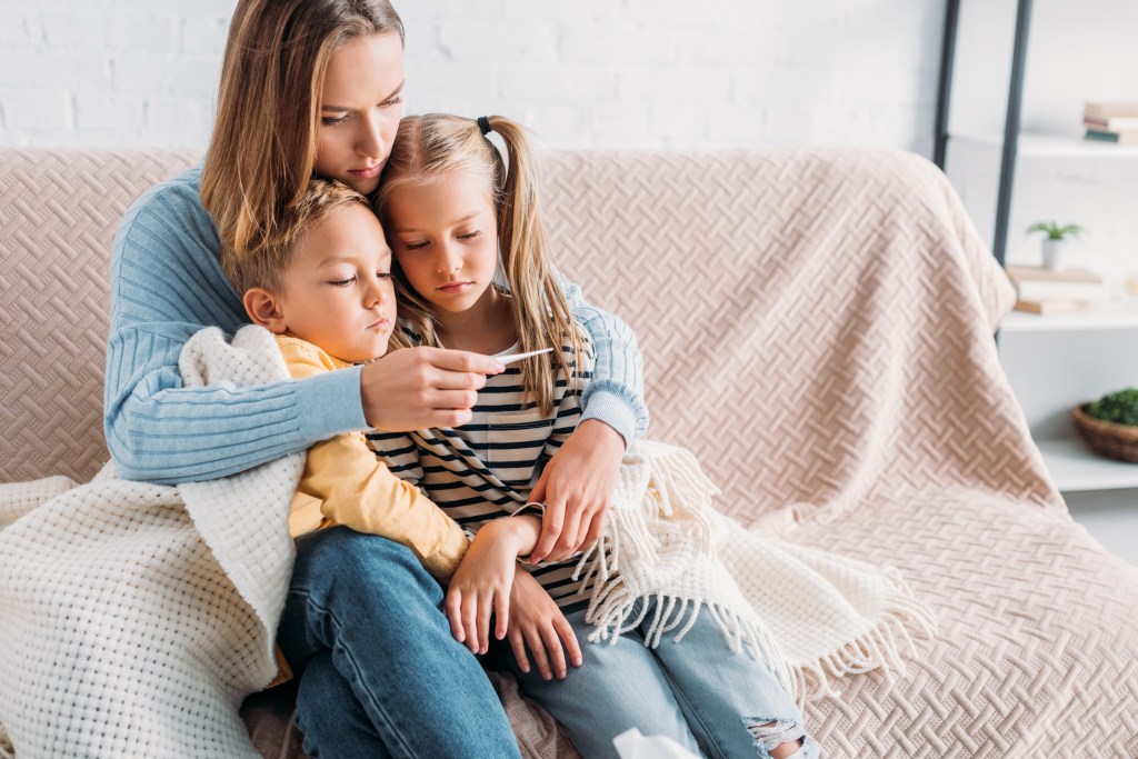 upset woman looking at thermometer while sitting on sofa with sick child