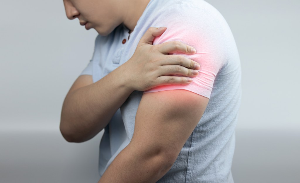 A man experiencing muscle pain, holding his shoulder with a red spot of inflammation, healthcare concept