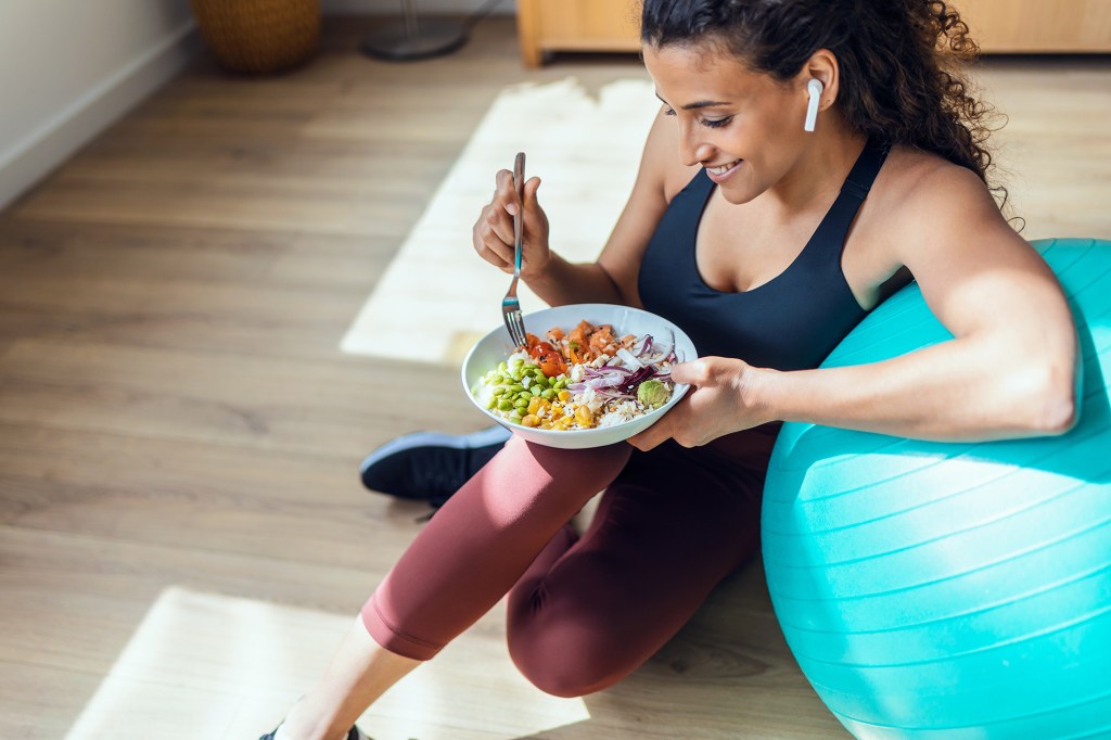 You don't need to spend a lot of money on the latest programs to get the best weight loss results. Here, a woman eats a healthy bowl of food while resting her arm on an exercise ball.