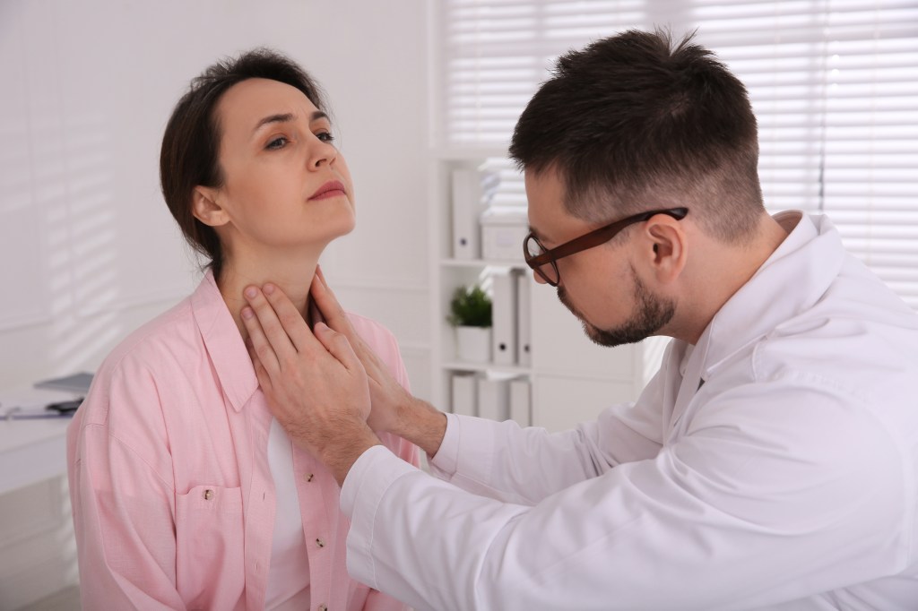 Doctor examining patient's thyroid gland in hospital.