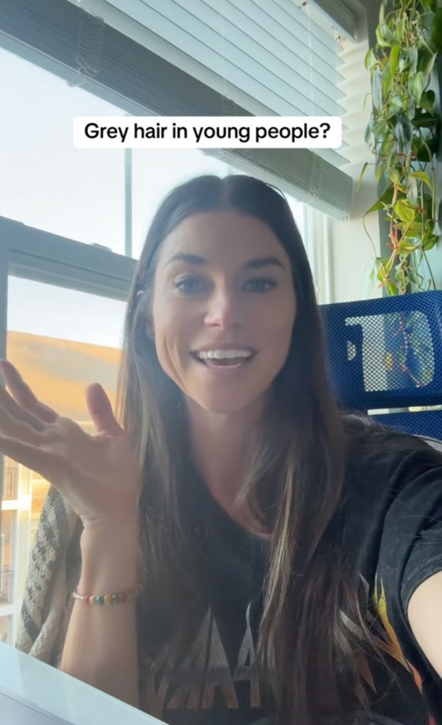 A woman with long hair and a black shirt discusses why Gen Z is going gray in a TikTok video