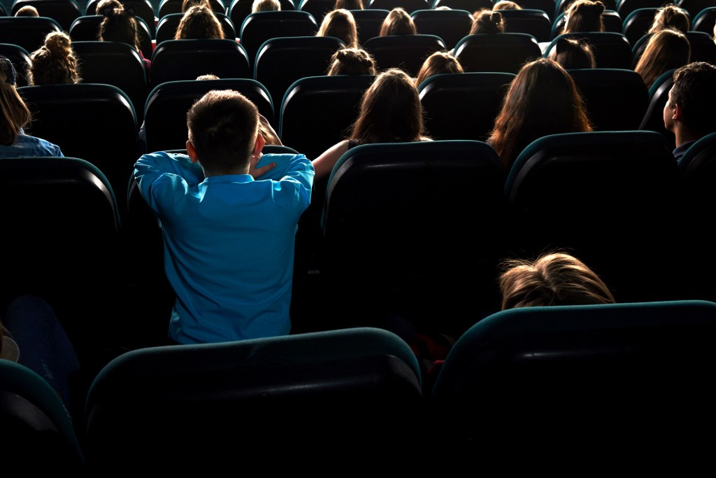 Back view of children intently watching a movie in a dark cinema auditorium